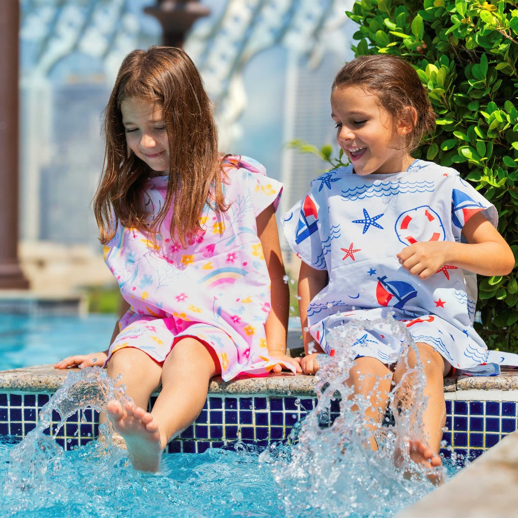 Boy and girl wearing La Toalla beach poncho for kids splashing their legs in the water
