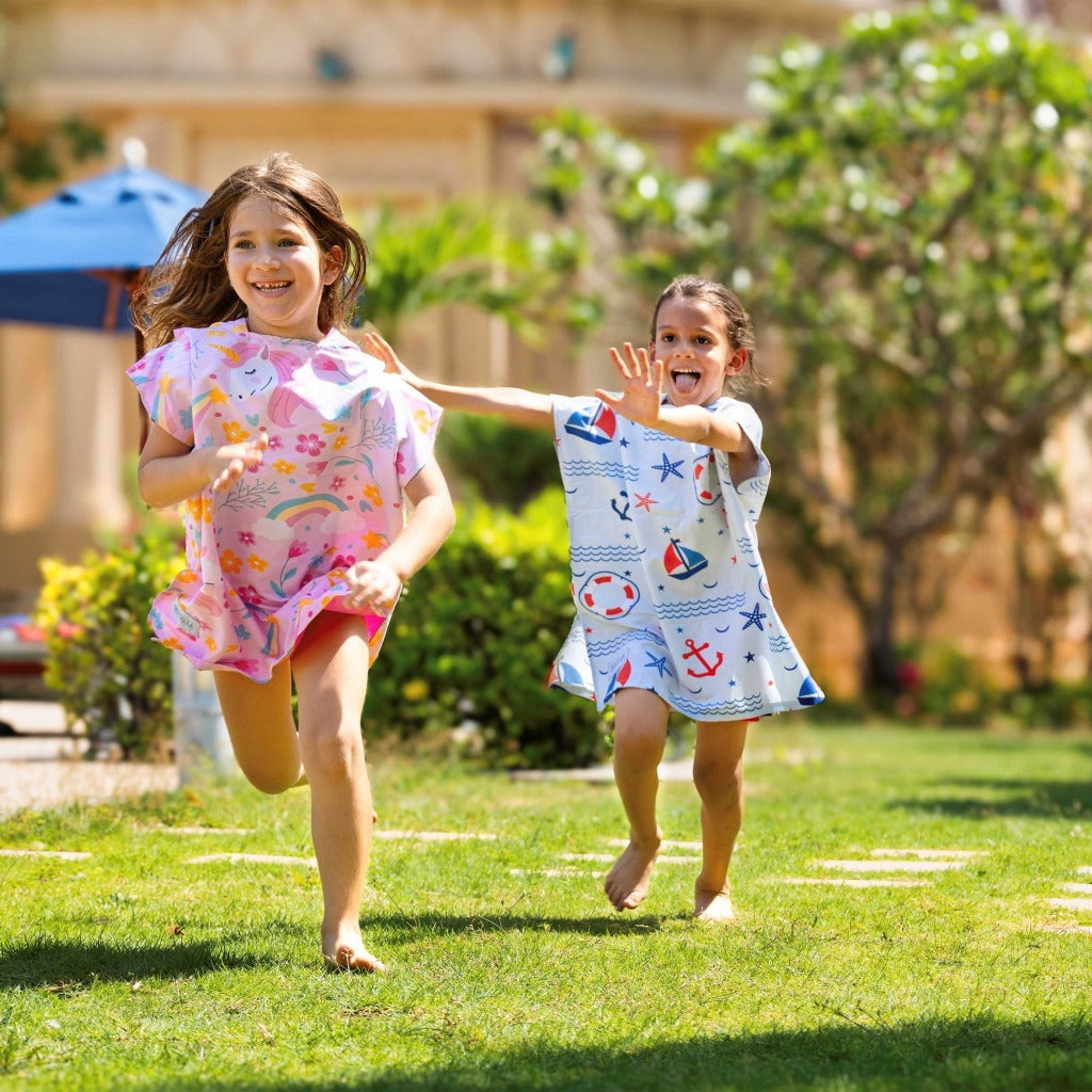 Boy and girl wearing La Toalla beach poncho for kids running around in the garden
