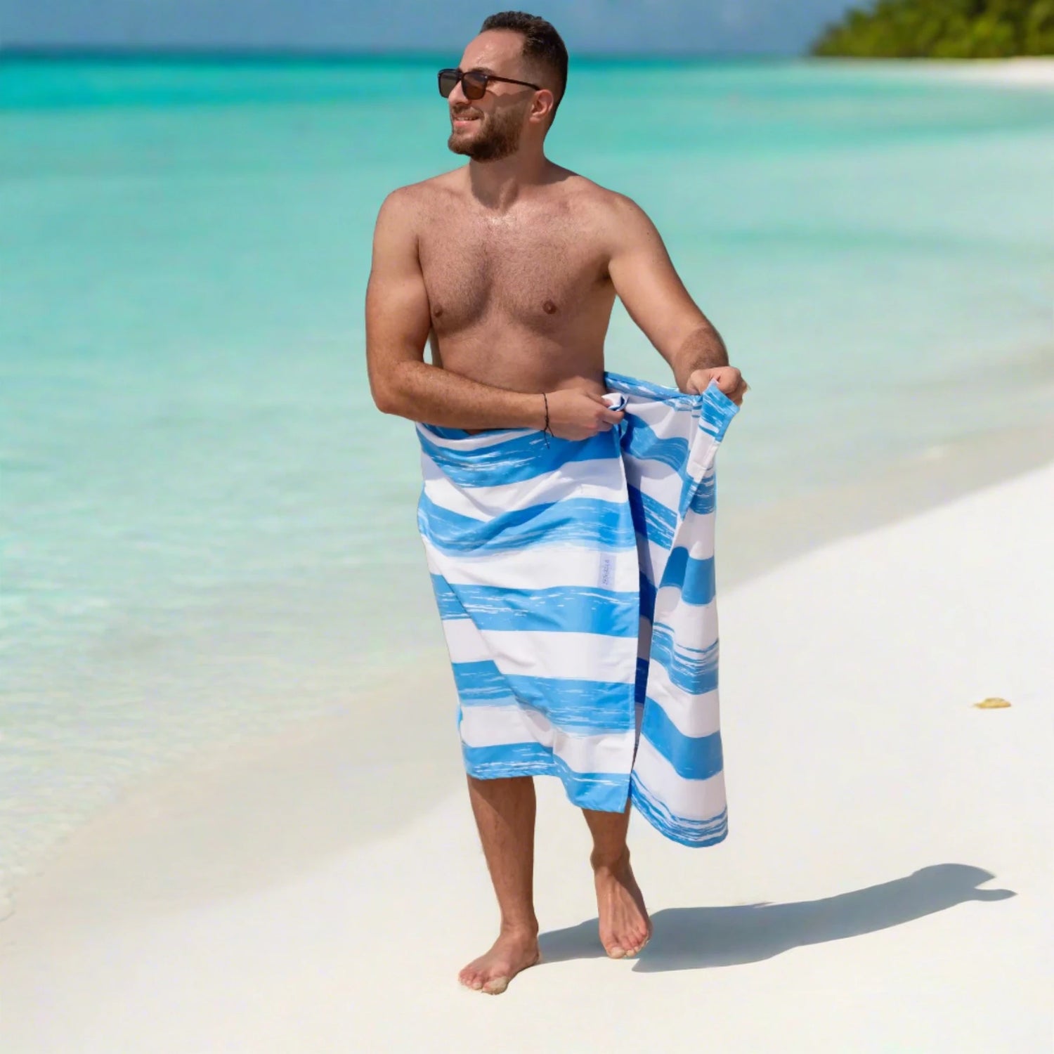A guy wrapping himself with a Quick Dry, Sand Free, Light Weight, Compact and Ecofriendly Microfiber Beach Towel from La Toalla