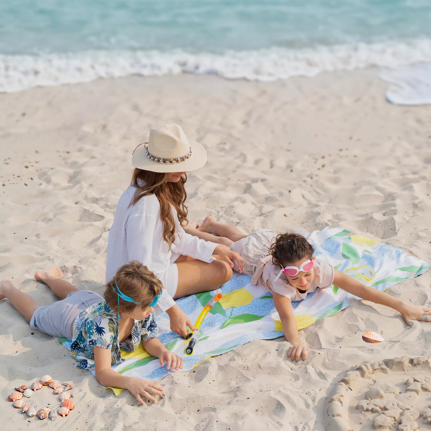 A mom and her kids sitting on a Quick Dry, Sand Free, Light Weight, Compact and Ecofriendly Microfiber Beach Towel from La Toalla on the sand