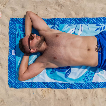 A guy lounging on a Microfiber Beach Towel from La Toalla on the sand