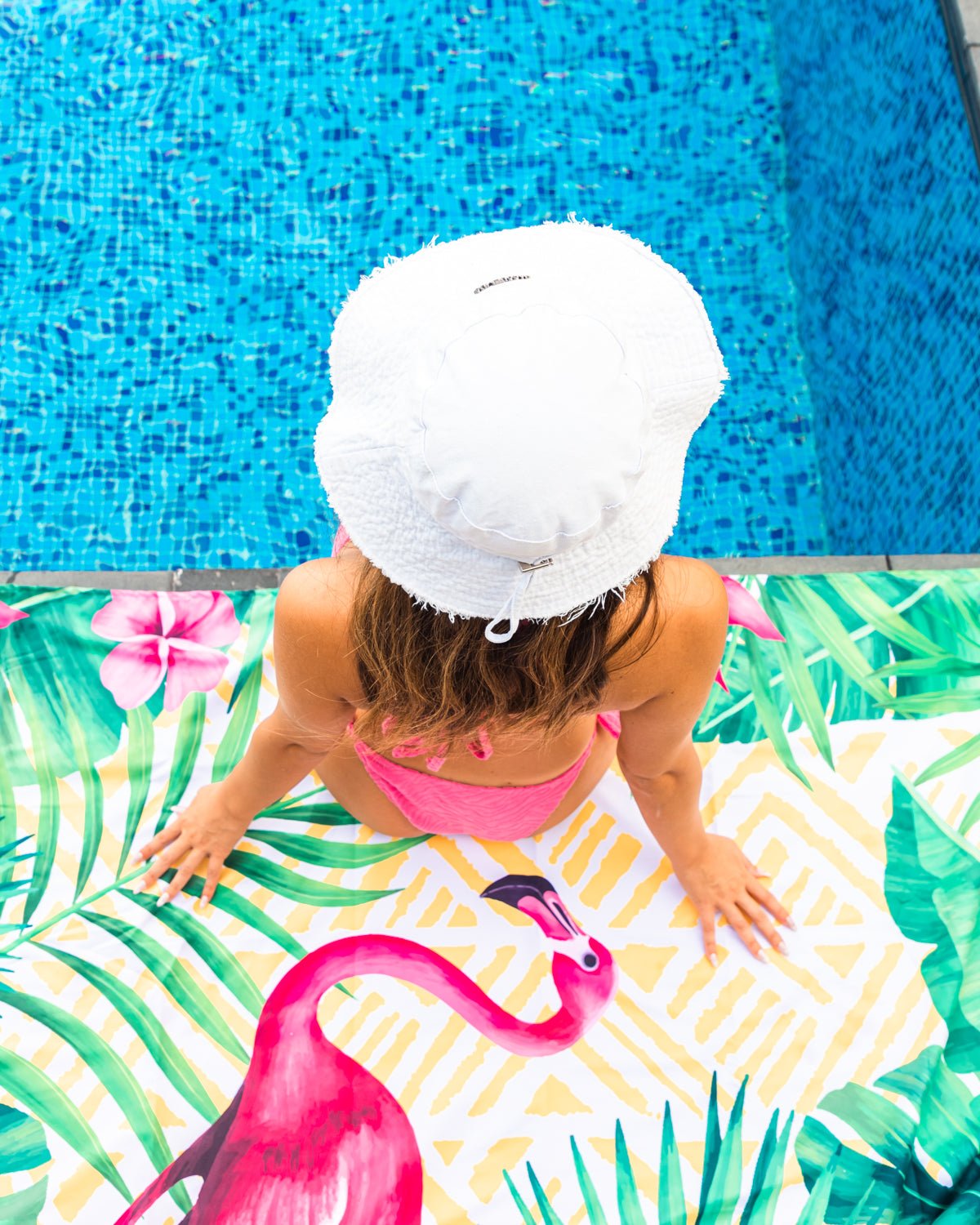 A girl sitting on the pool on a Quick Dry, Sand Free, Light Weight, Compact and Ecofriendly Microfiber Beach Towel from La Toalla